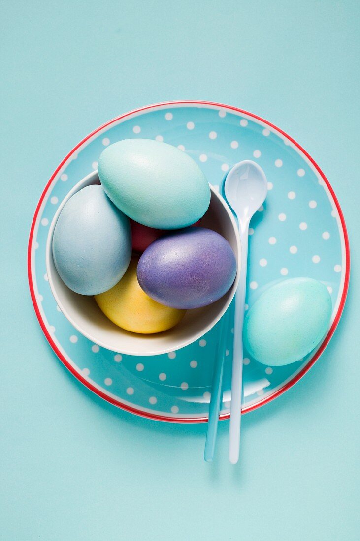 Coloured eggs in a white bowl on a plate with a spoon