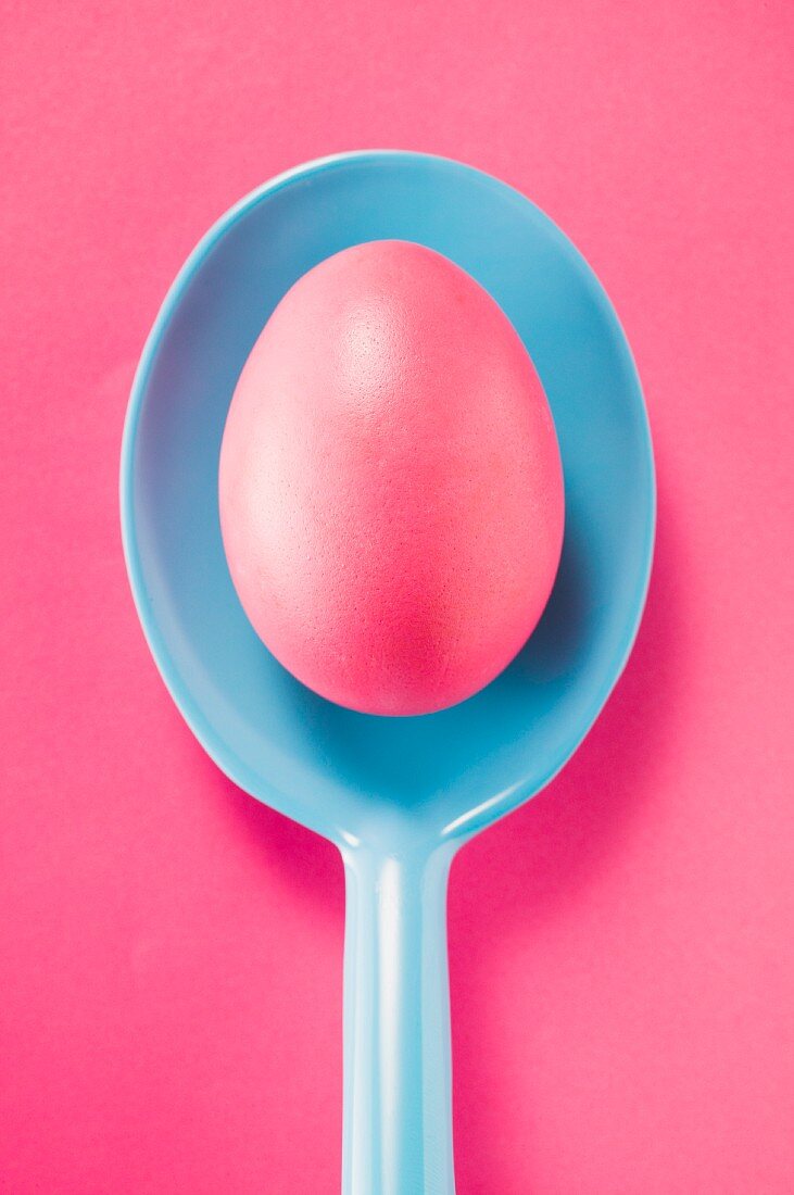 A pink Easter egg on a blue plastic spoon (seen from above)