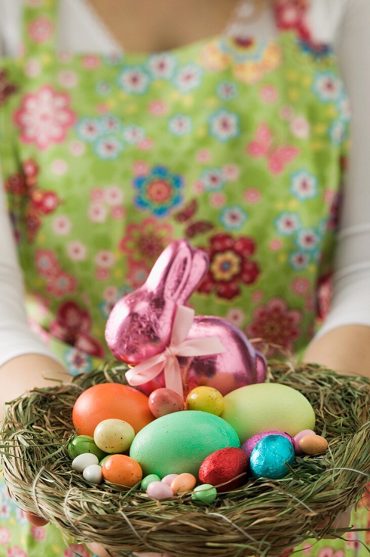 Frau hält Osternest mit gefärbten Eiern und Süssigkeiten