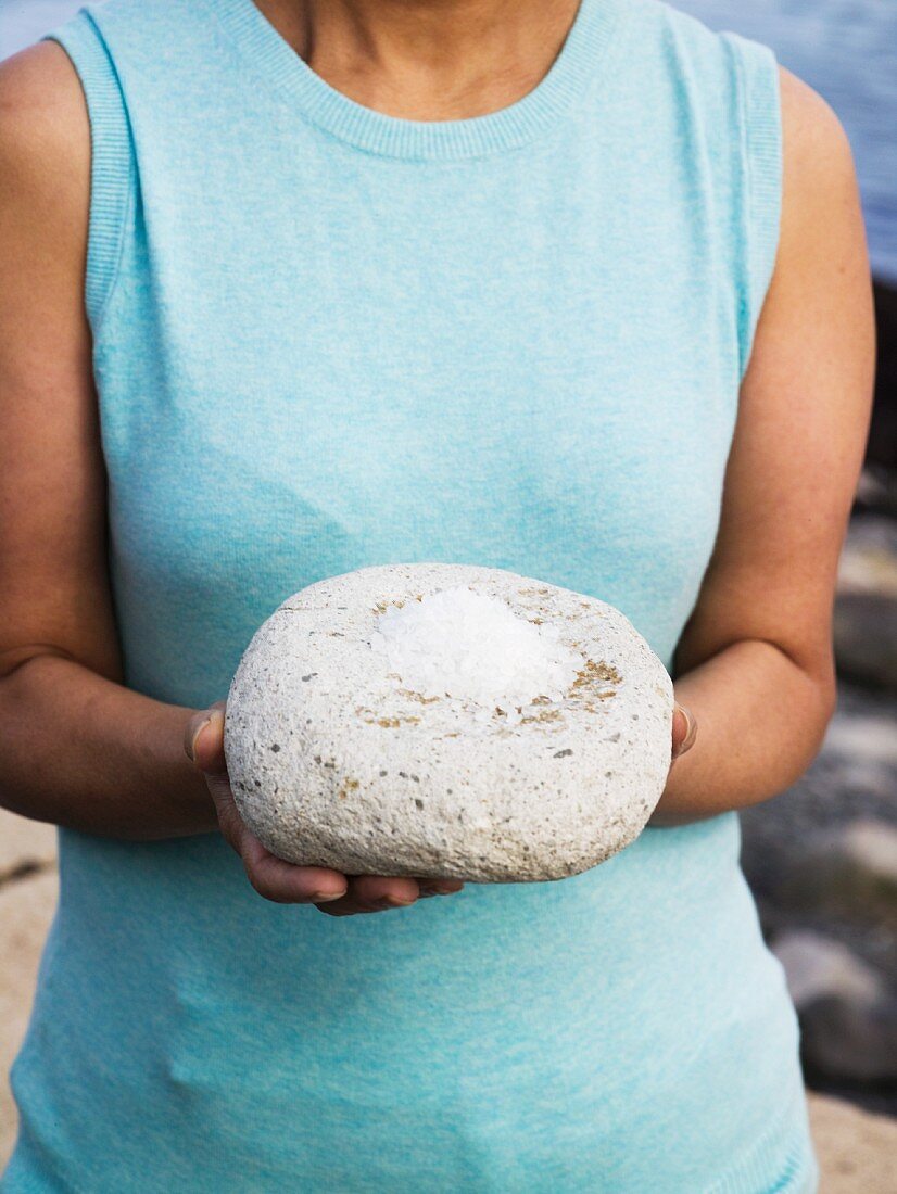 Frau hält Meersalz auf grossem Stein