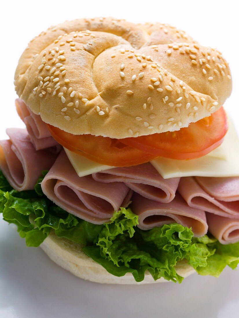 A sesame seed roll with ham, cheese and tomato (close-up)