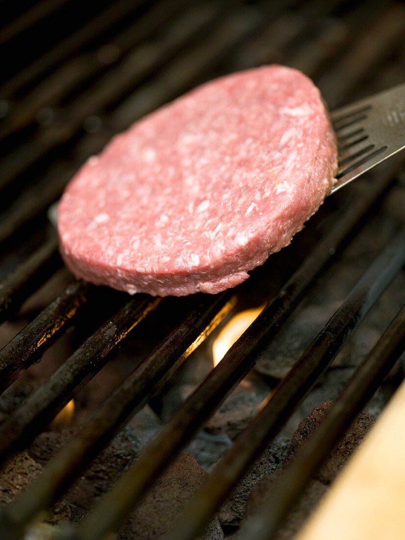 A raw burger being place on a barbecue