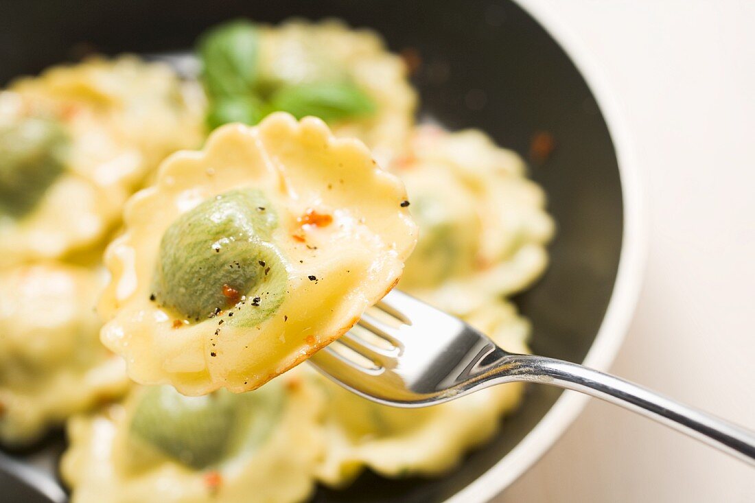 Spinach ravioli on a fork over a pan