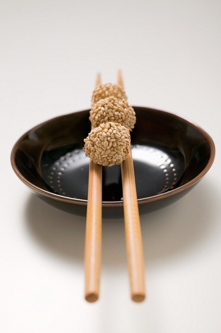 Three rice balls with sesame seeds on chopstick over a plate