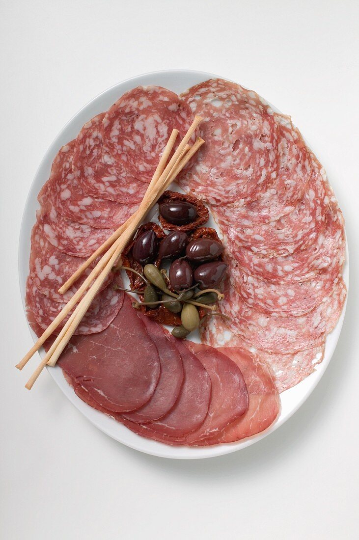 A meat platter with olives, capers and breadsticks (Italy)