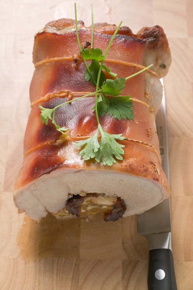 Stuffed roast pork on a chopping board with a knife