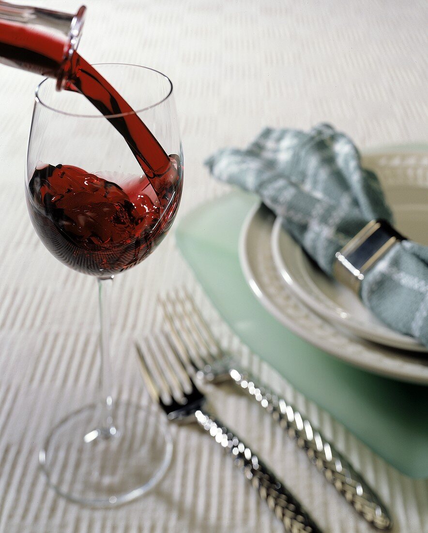Rotwein in Glas einschenken neben Gedeck auf Tisch