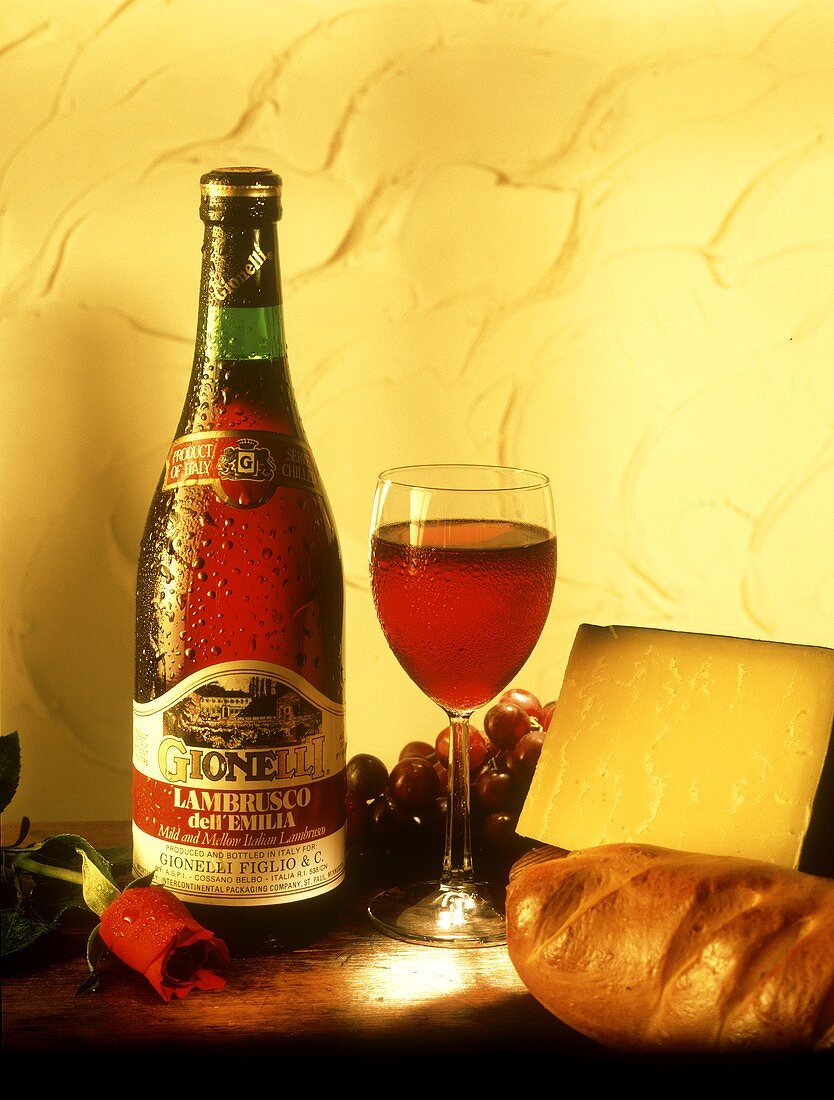 Eine Flasche Lambrusco neben Rotweinglas, Käse, Weißbrot