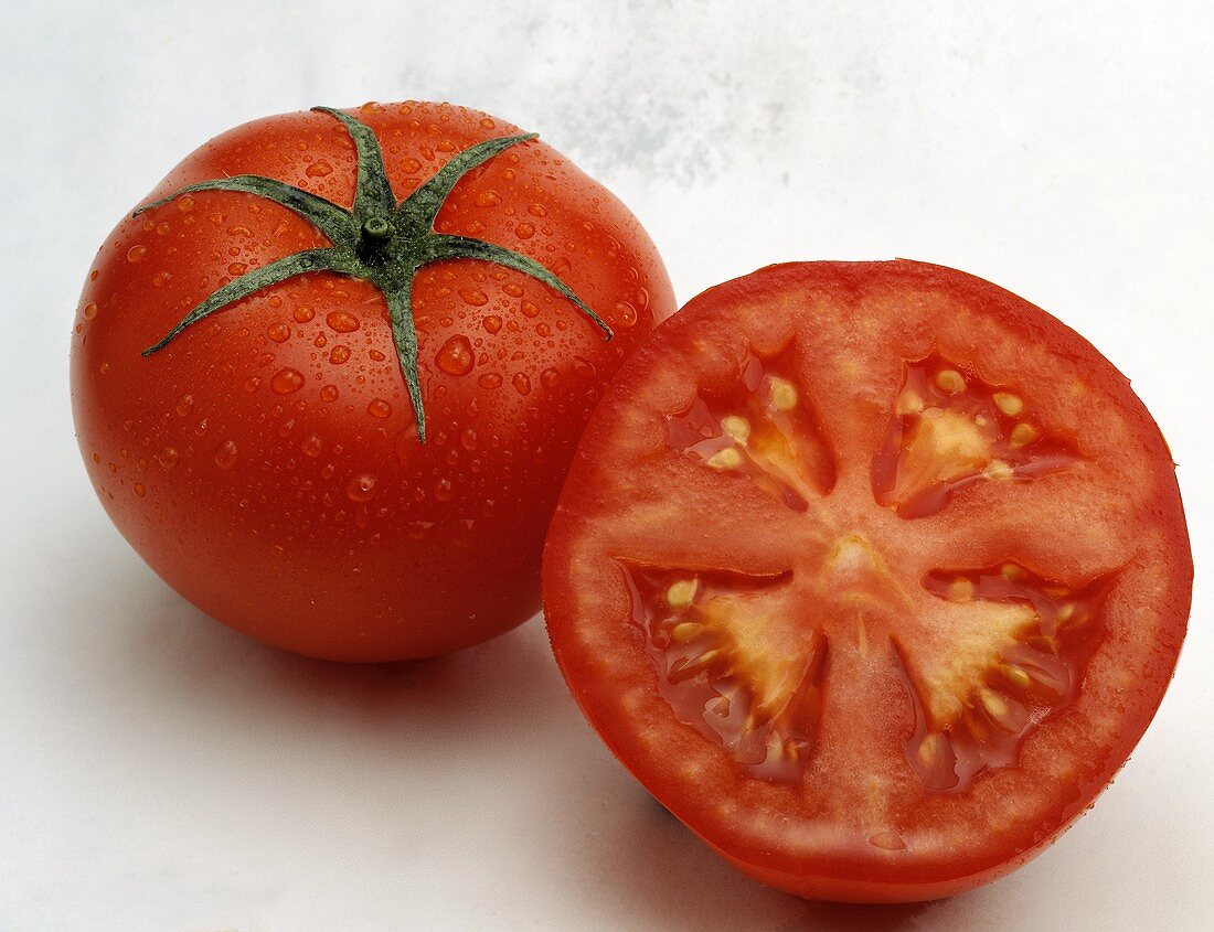 Tomate mit Wassertropfen und Tomatenhälfte