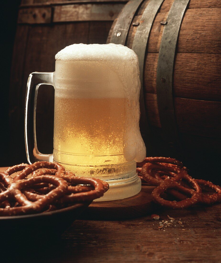 Ein Krug mit hellem Bier; Brezel und Bierfass