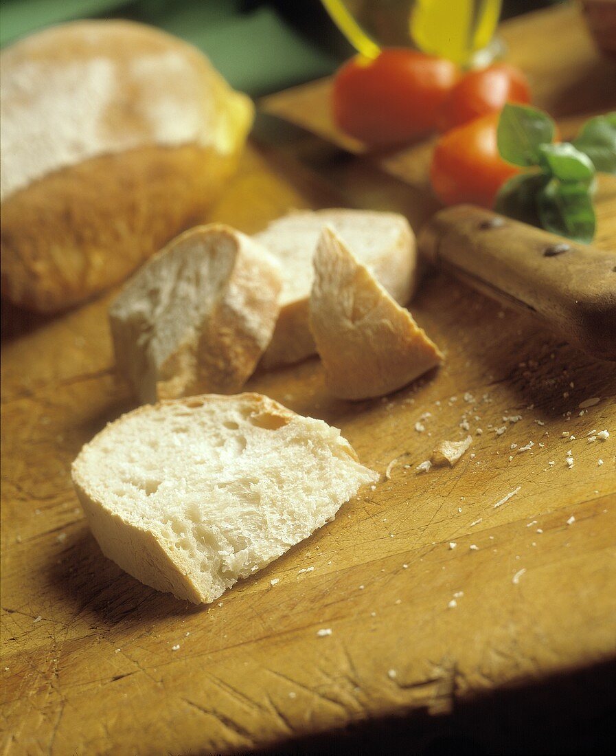 Weißbrot mit Brotscheiben auf Holzbrett; Tomaten; Basilikum