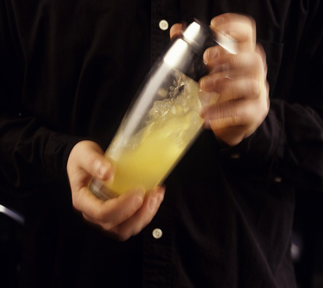 Mann schüttelt Cocktailshaker aus Glas