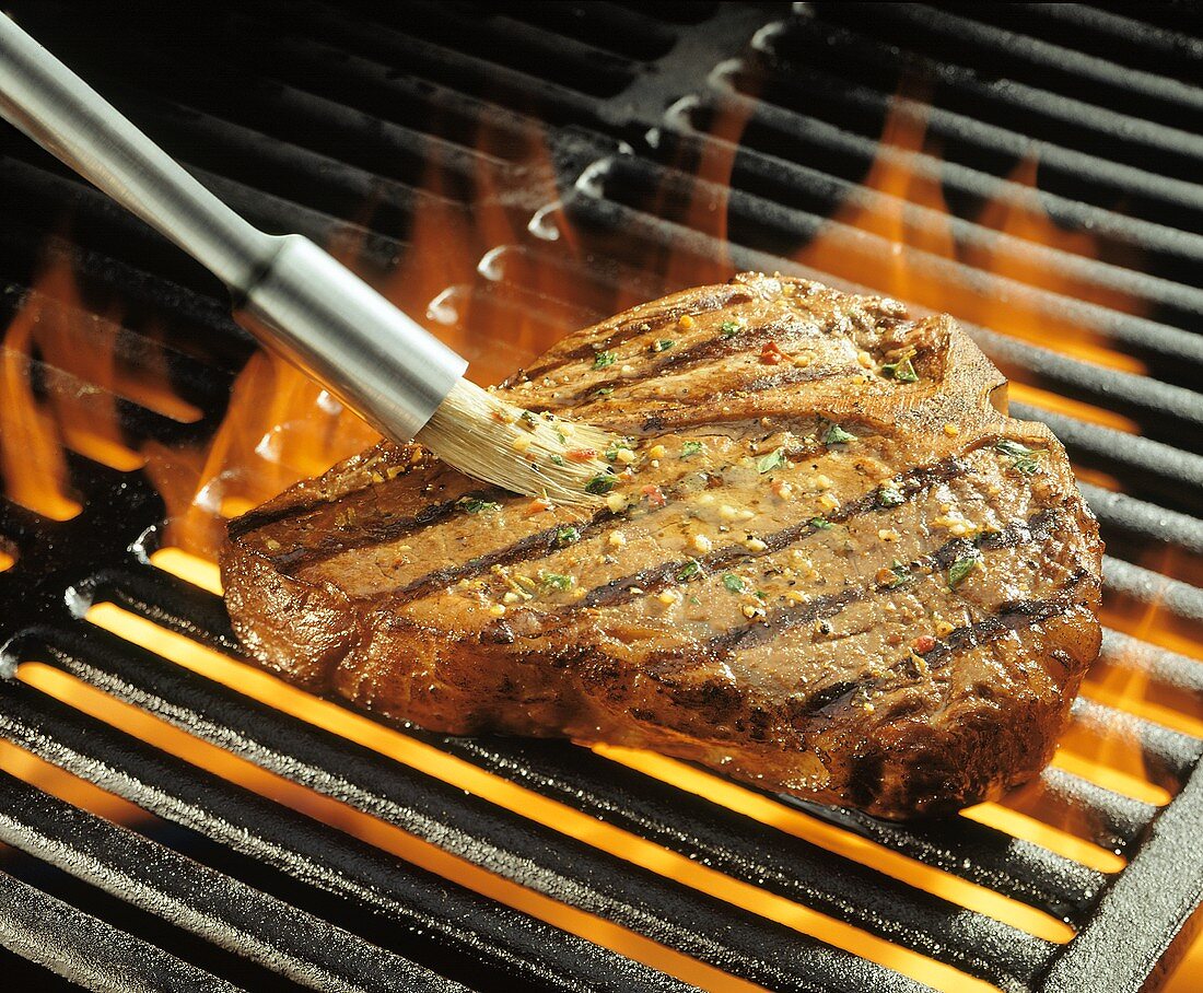 Steak auf dem Grill mit Marinade bestreichen