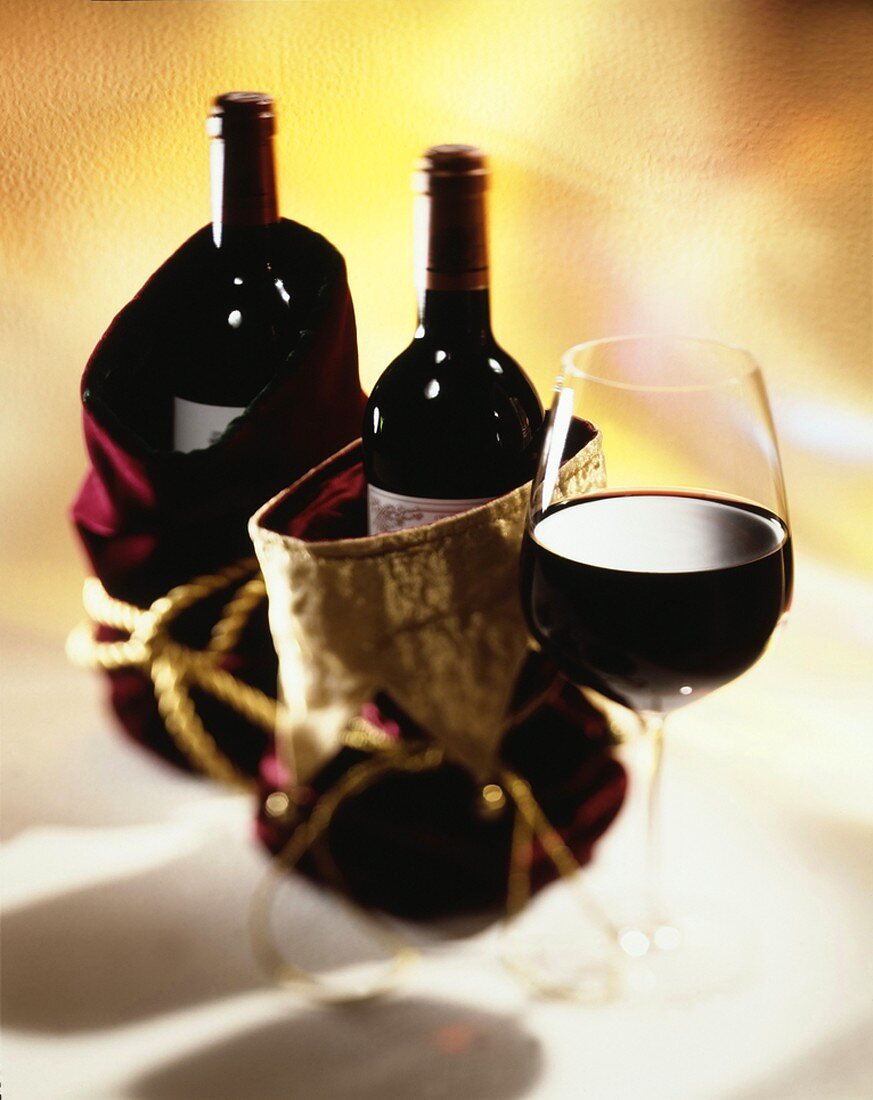 Rotweinflaschen in Geschenkbeuteln, daneben Rotweinglas