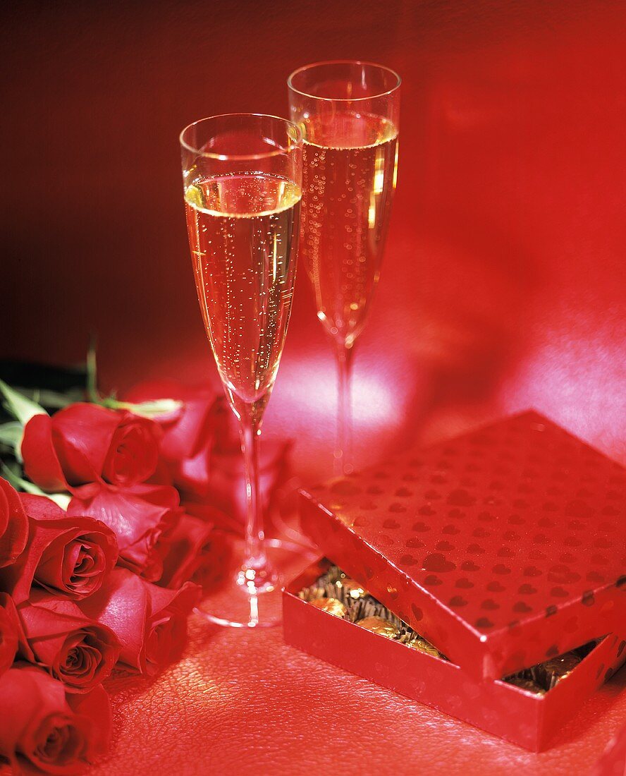 Two Flutes of Champagne, Roses and Candy on a Red Background