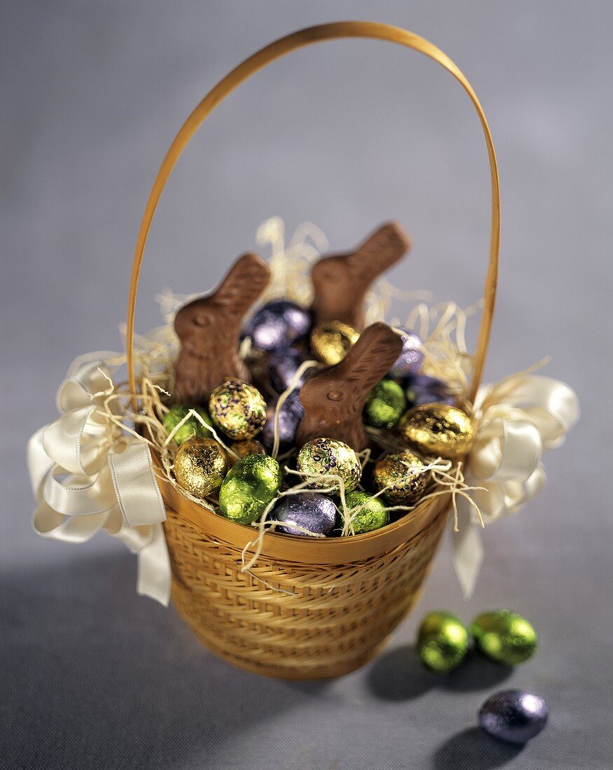 Easter Basket with Chocolate Bunnies and Foil Wrapped Eggs on Lavender Background