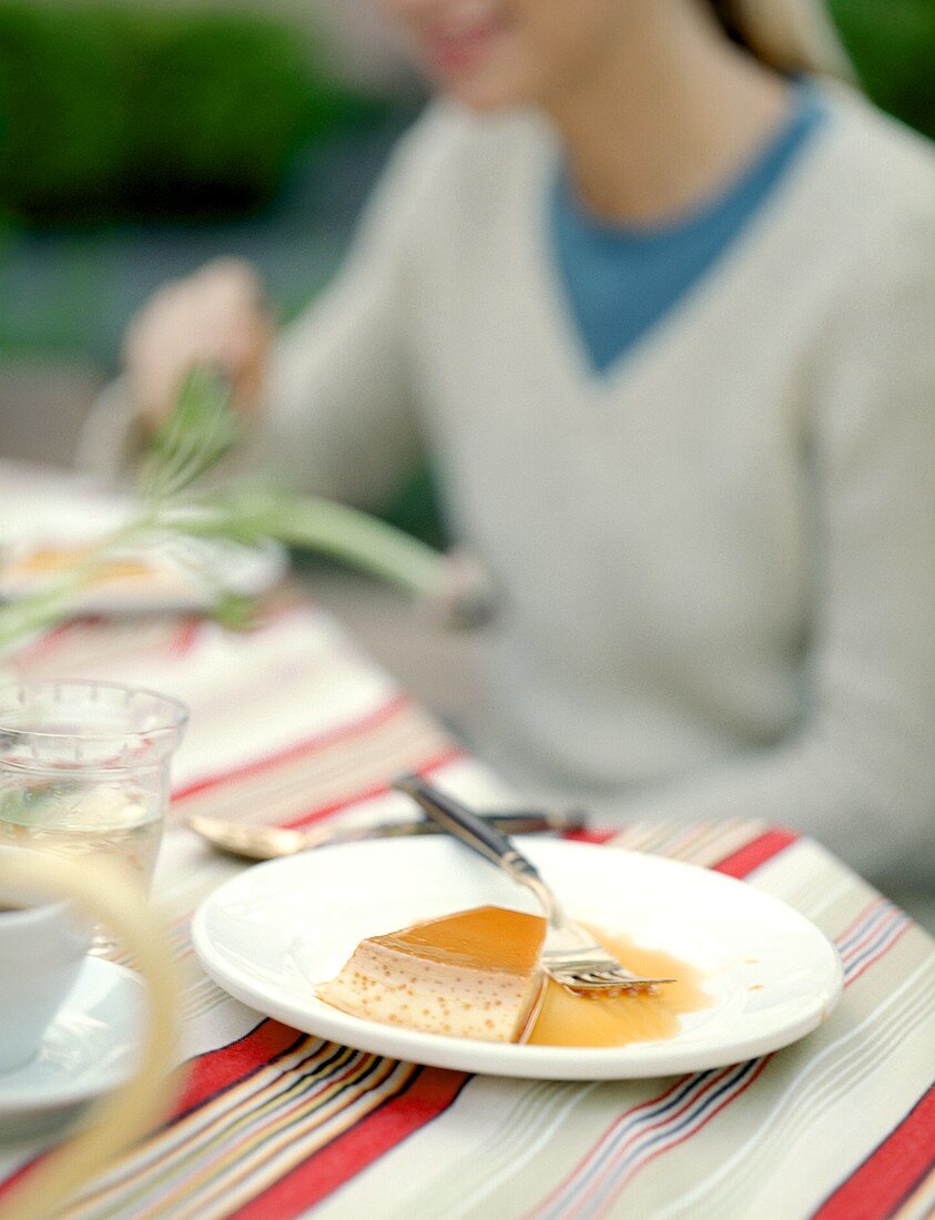 Flan mit Karamellsauce auf Tisch; Frau im Hintergrund