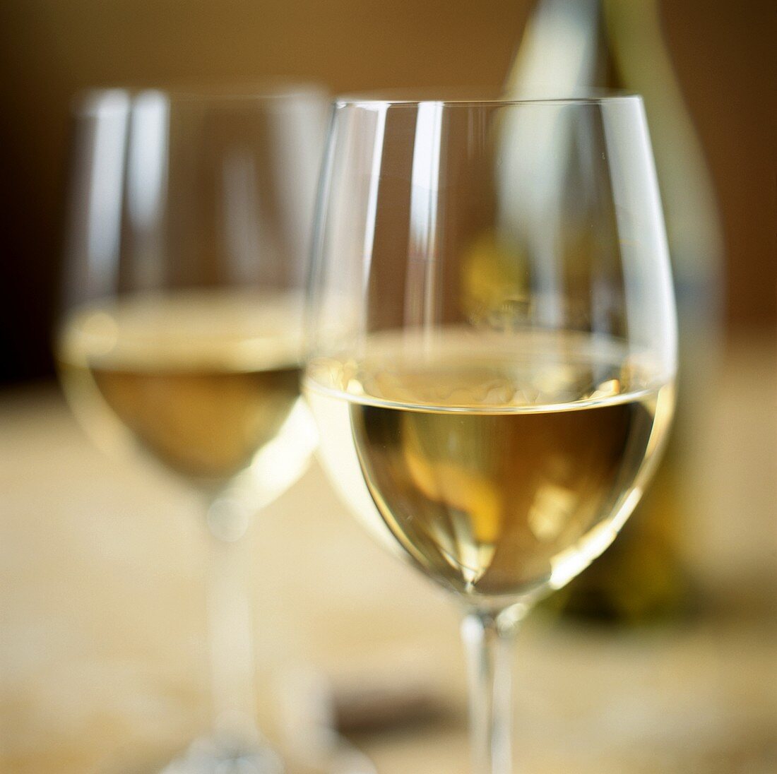 Two white wine glasses in front of bottle in background