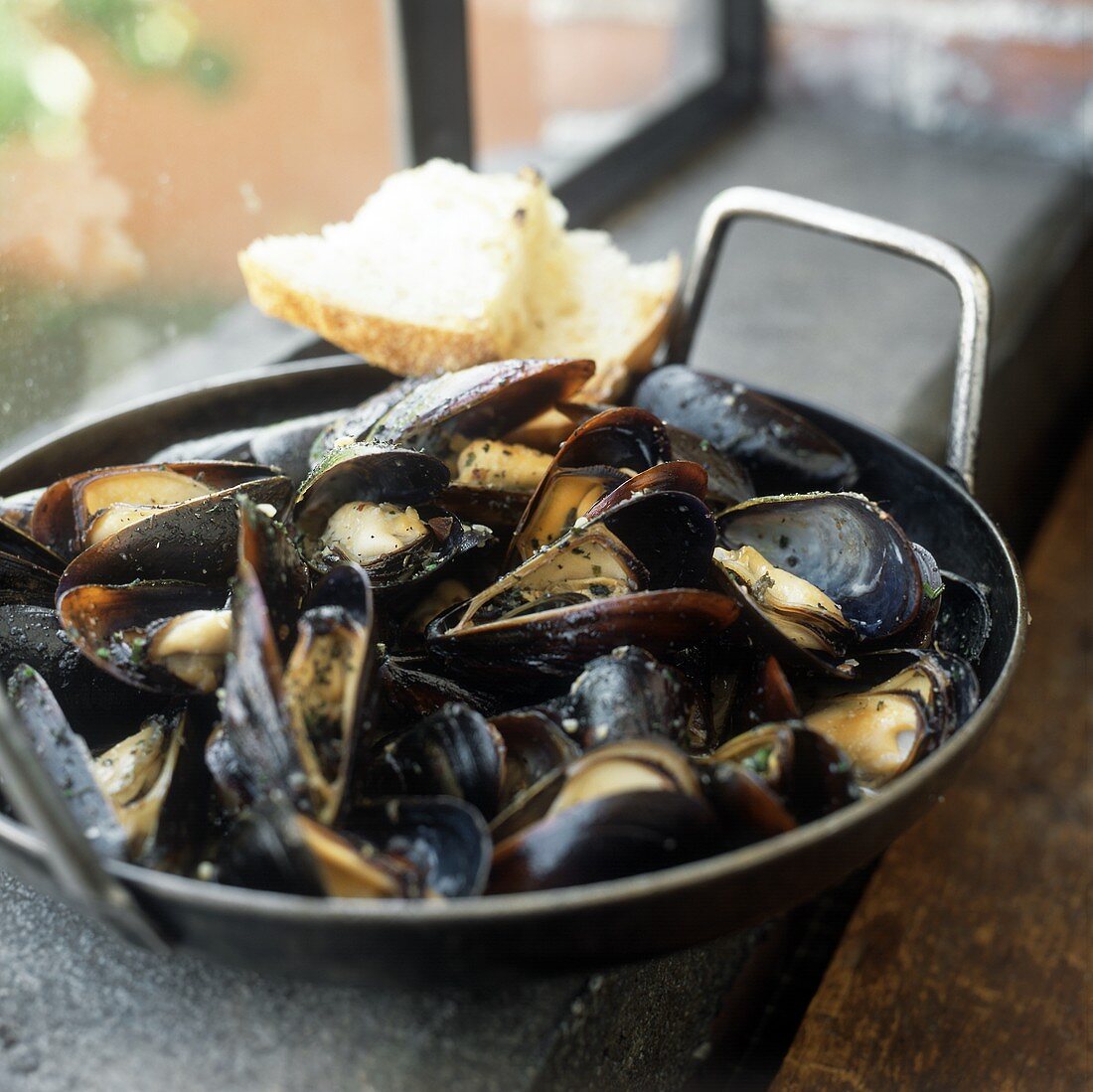 Steamed mussels with herbs in frying pan; white bread