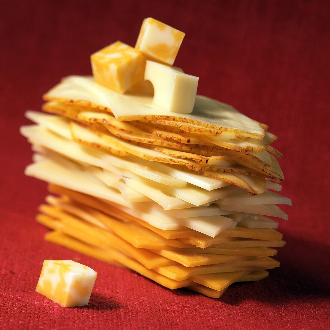 Ein Stapel Scheiben verschiedener Sorten Käse und Käsewürfeln