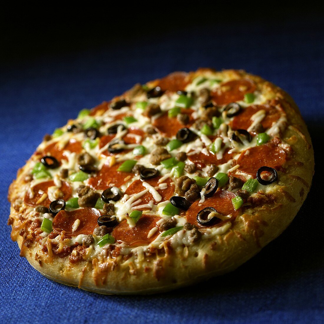 Pizza mit Paprika, Oliven und Salami auf blauem Untergrund