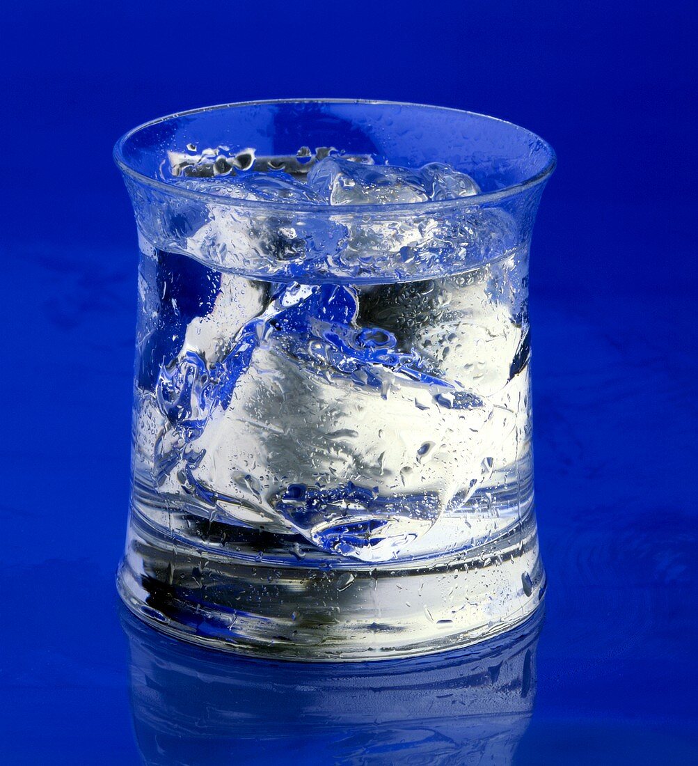 Glas Wasser oder Gin Tonic mit Eis vor blauem Hintergrund