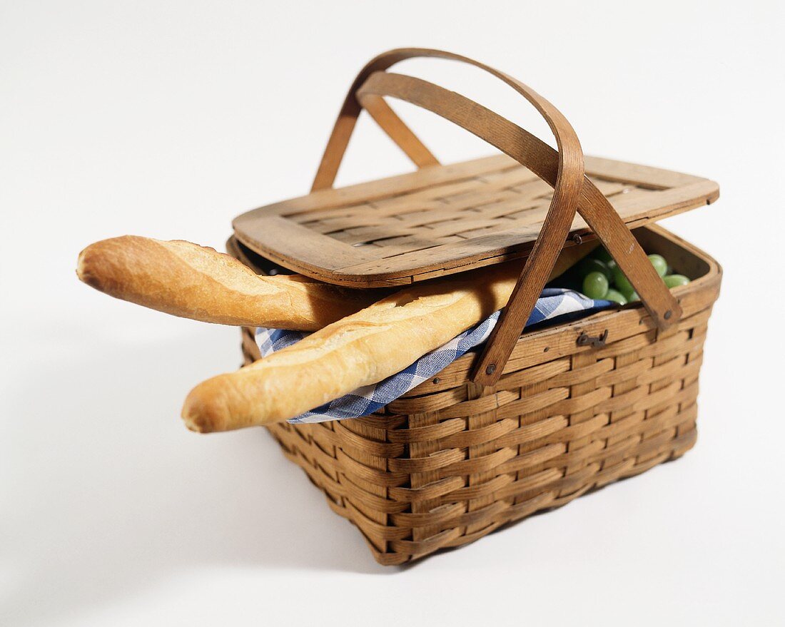 A Picnic Basket with Two Baguettes and Green Grapes