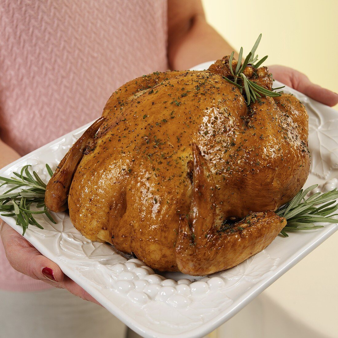 Hands Holding Roast Chicken on a White Platter