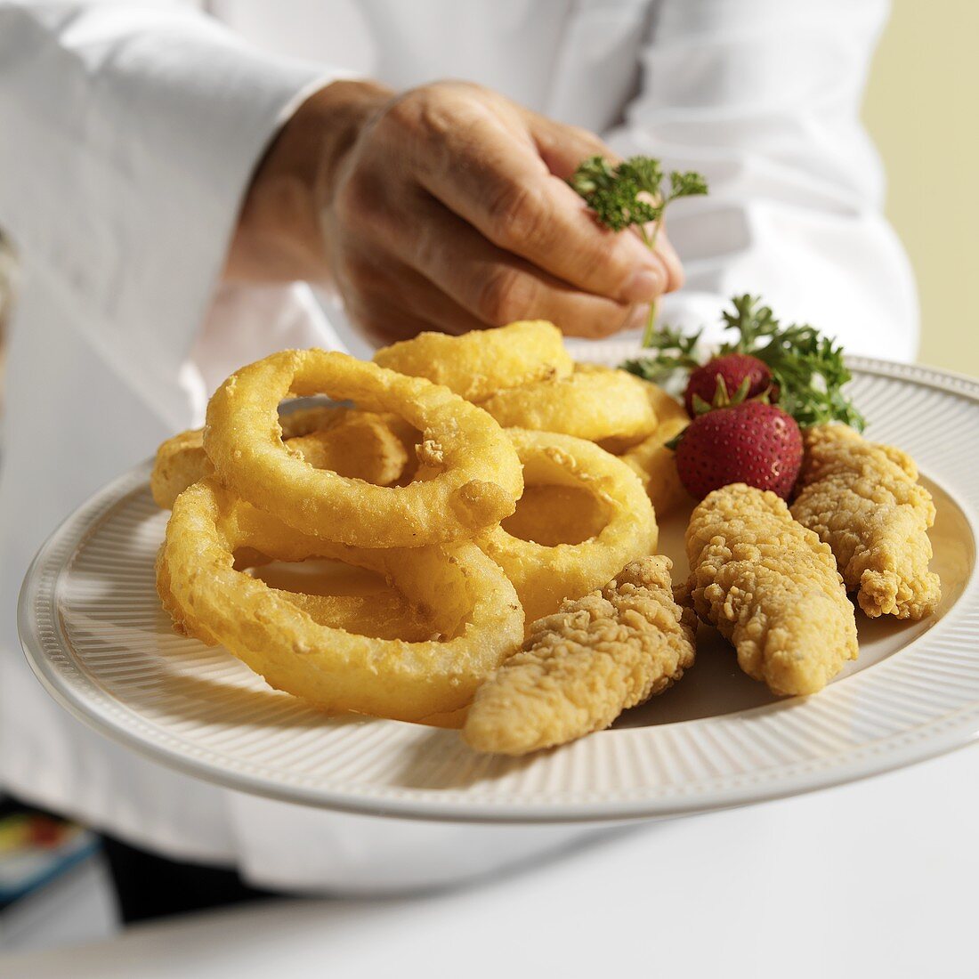 A Chef Placing a Parsley Garnish on a Plate of Chicken Tenders and Onion Rings