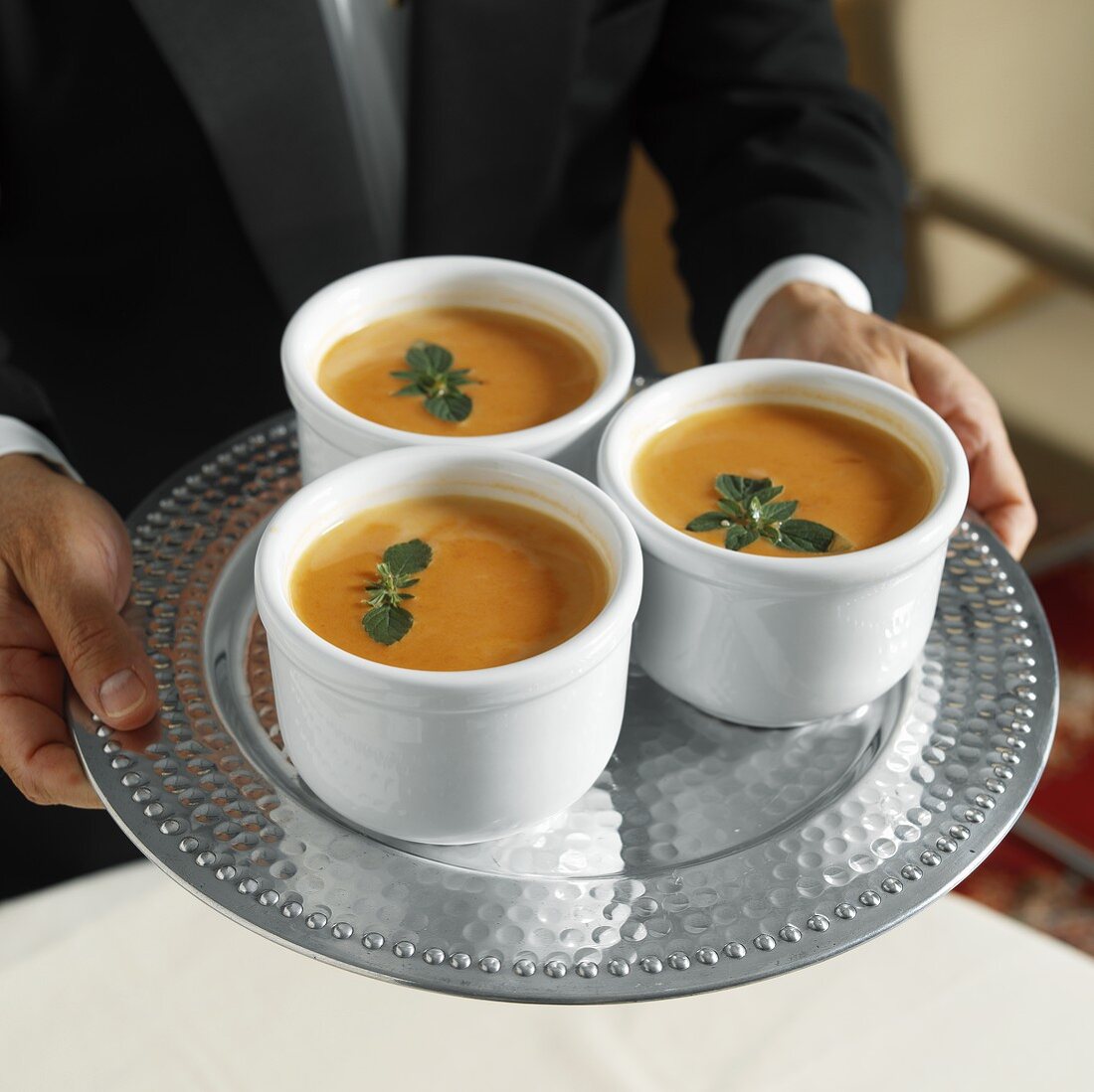 A Waiter Serving Three Bowls of Cream of Tomato Soup with Oregano