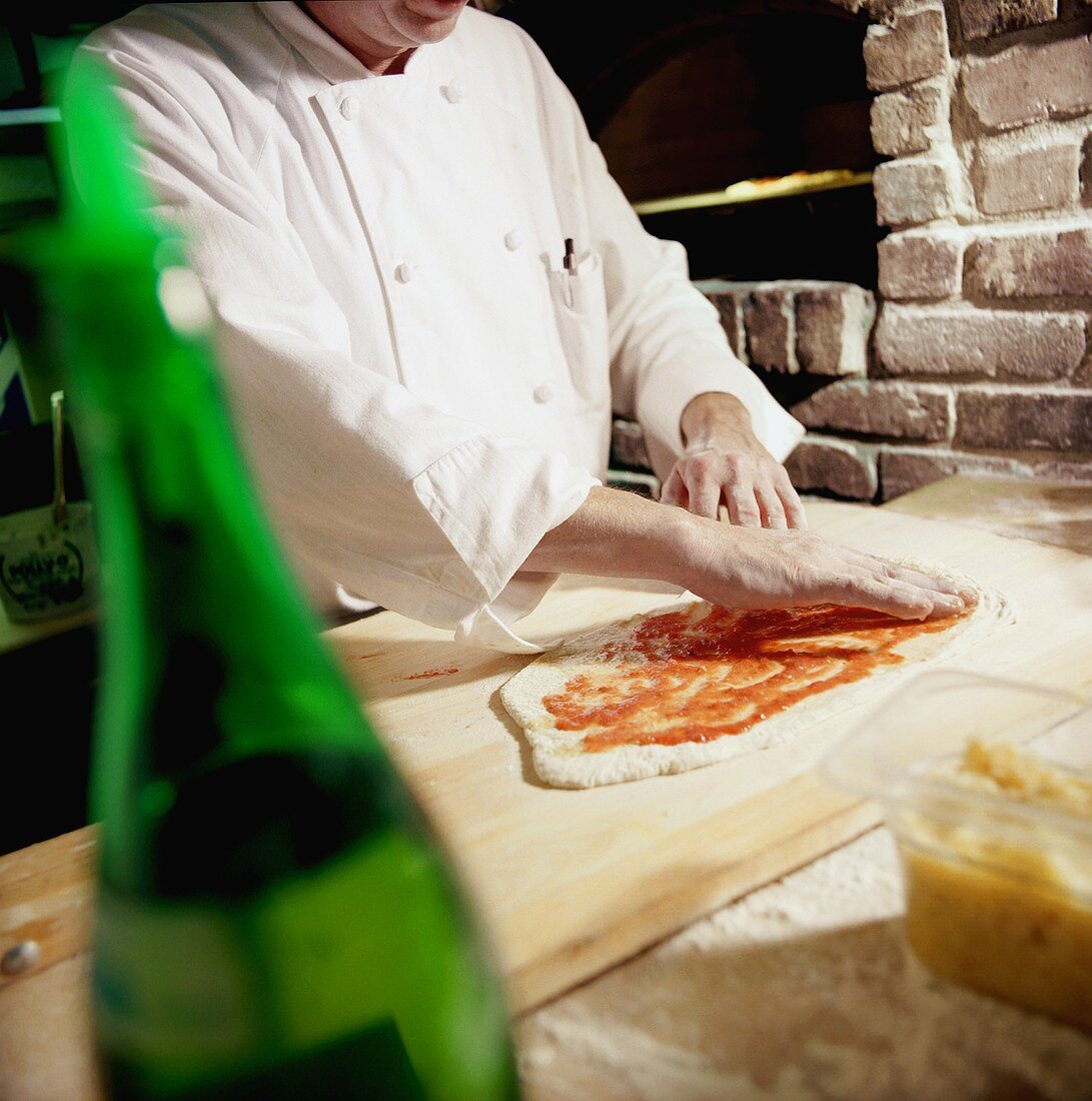 Chef Spreading Tomato Sauce on Pizza with Hands