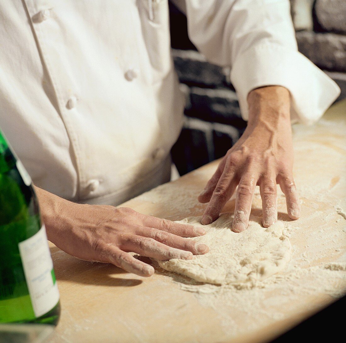 Chef Flattening Pizza Dough with His Hands