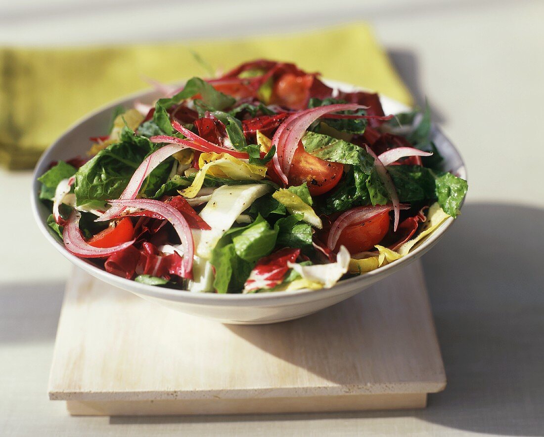 A Tossed Salad with Lettuce, Red Onion and Tomato on a Wooden Board