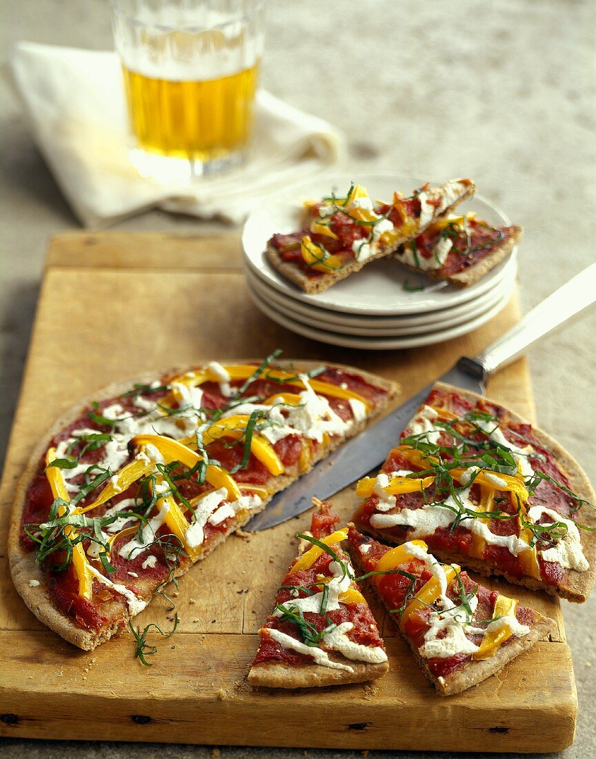 Pizza with tomatoes, peppers and basil on chopping board