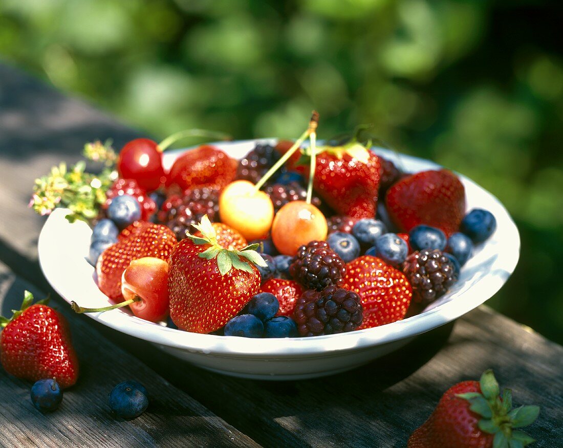 Plate of fresh summer fruits on table in open air
