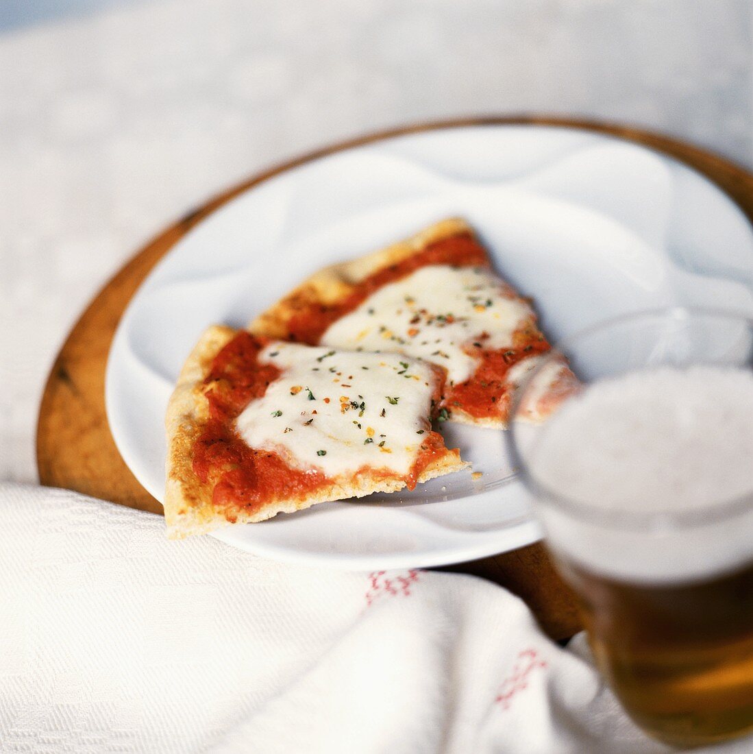 Zwei kleine Stückchen Pizza auf Teller, davor Glas mit Bier