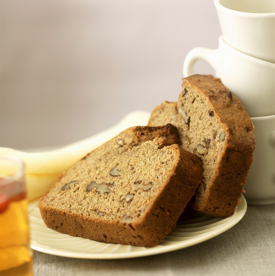 Two slices of banana and walnut bread beside coffee cups