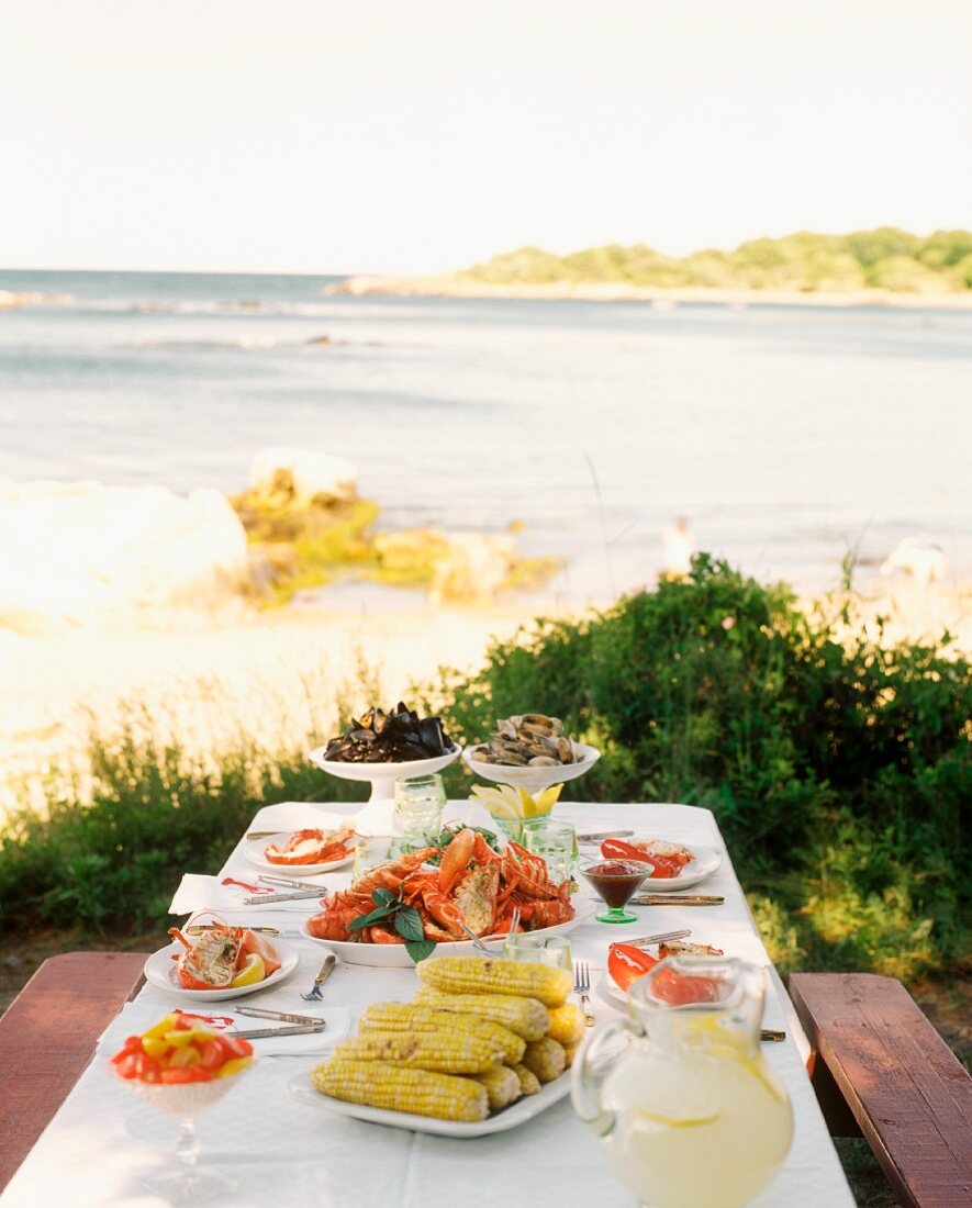 Gedeckter Tisch am Meer mit Hummer, Muscheln und Maiskolben