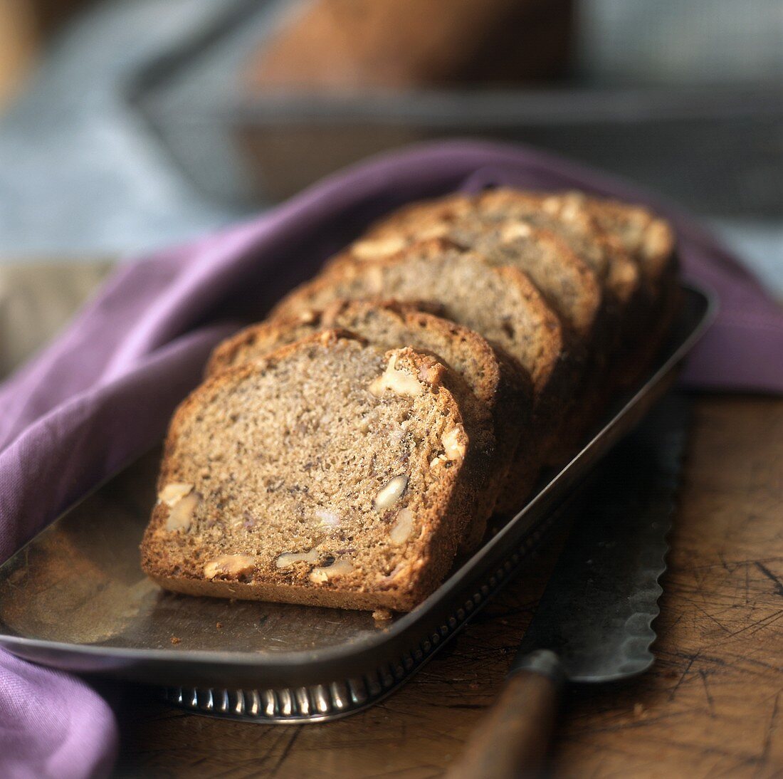 A Sliced Loaf of Banana Nut Bread with a Knife and a Purple Napkin