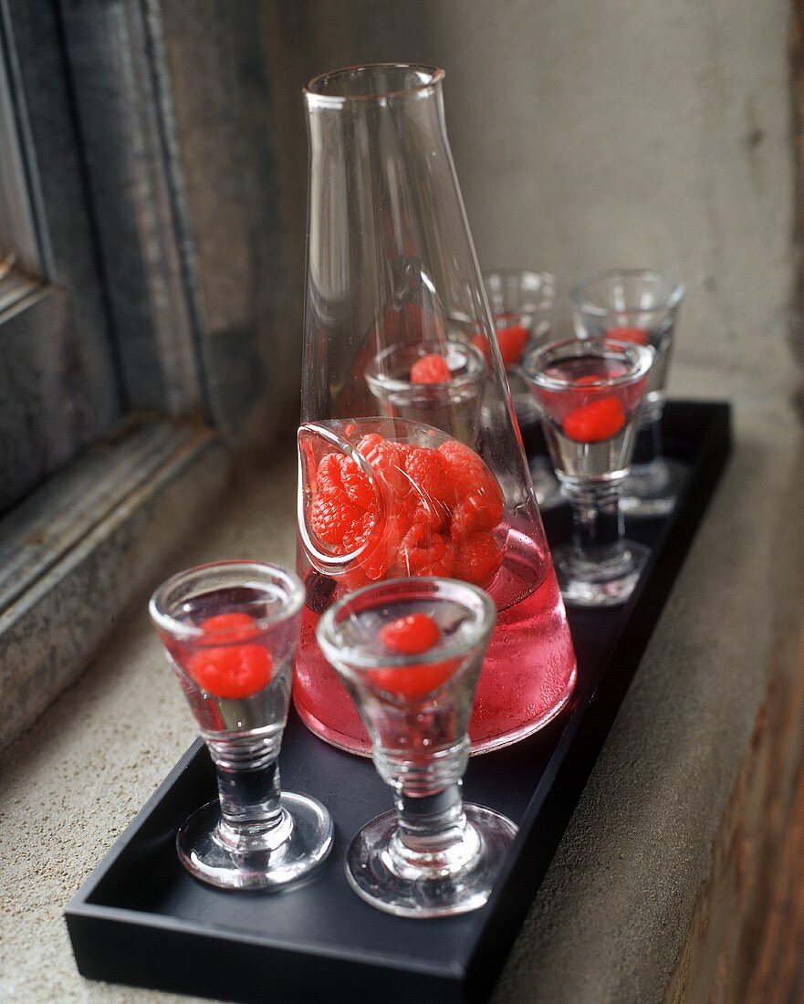 Raspberry cocktails in glasses and decanter on a rectangular tray by a window 