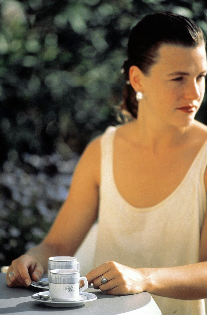 Junge Frau sitzt an einem Tisch mit zwei Espressotassen