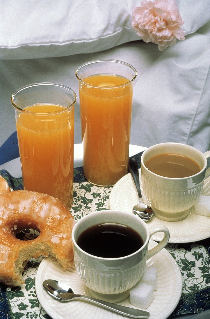 Frühstückstablett mit Kaffee, Orangensaft, Donut neben Bett