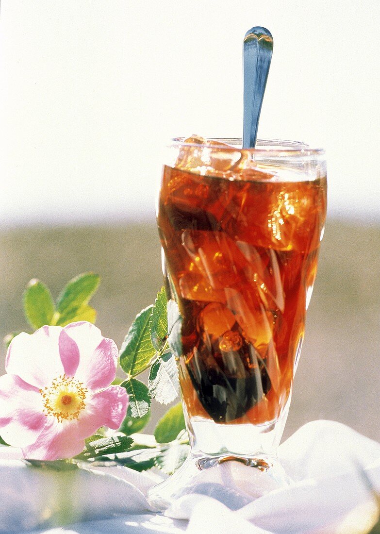 Glas kalter Kaffee mit Eiswürfeln & Löffel, daneben Blumen