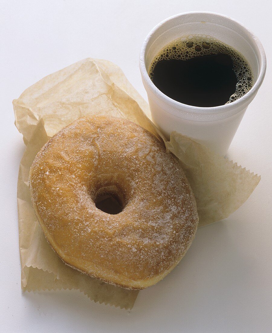 Ein gezuckertes Doughnut & ein Becher schwarzer Kaffee