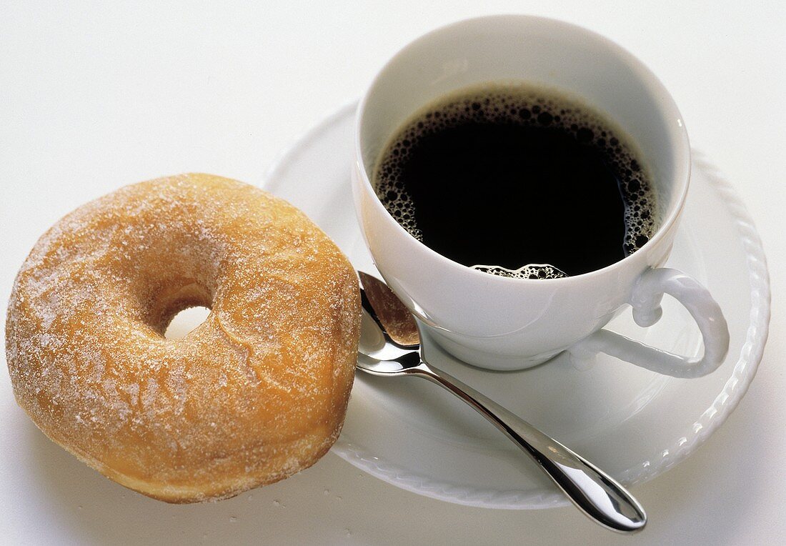 Ein gezuckertes Doughnut & eine Tasse schwarzer Kaffee