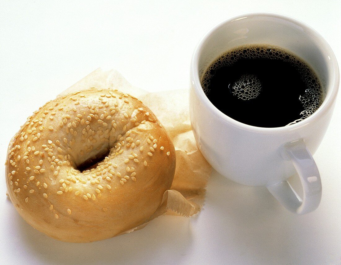 Ein Sesambagel auf Papier & eine Tasse schwarzer Kaffee