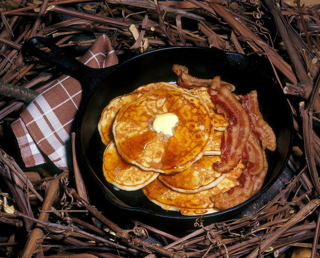 Pancakes mit Ahornsirup, Butter und Speck in Bratpfanne