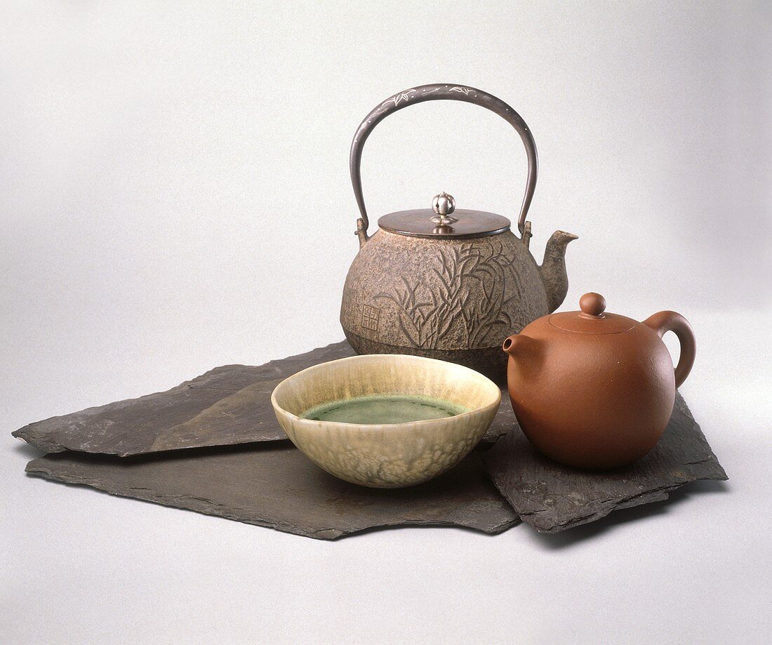 Grüner Tee in einer Schale vor zwei Teekannen