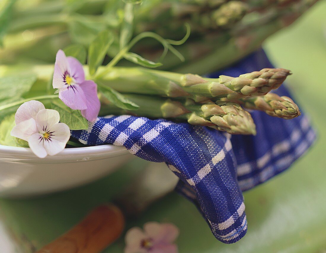 Grüner Spargel auf kariertem Tuch in Schale mit Blüten