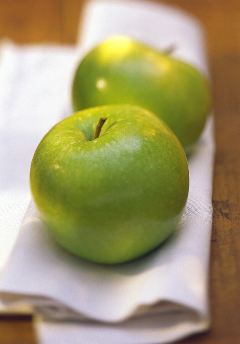 Zwei Äpfel der Sorte Granny Smith auf weißem Tuch